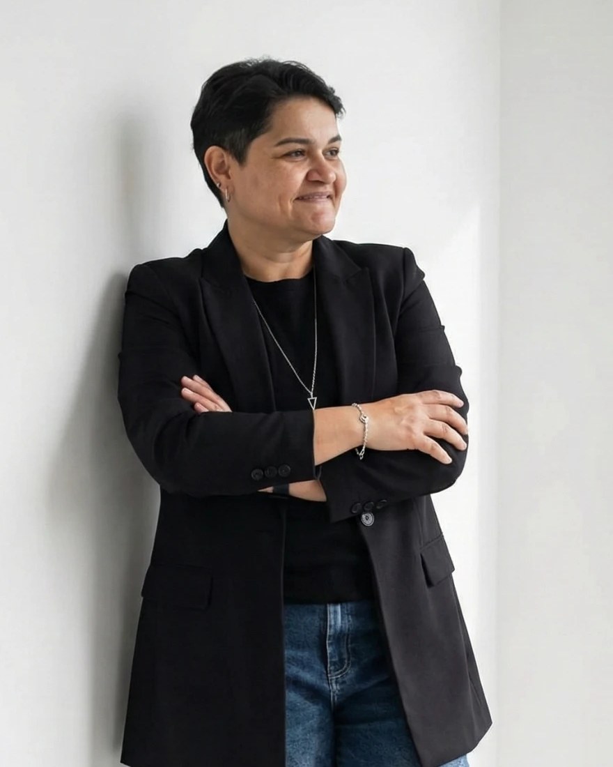 Jeane Marilá de blazer preto, encostada na parede, sorrindo